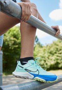 Chaussures de course bleu clair et vert avec une tige en mesh, semelle en caoutchouc et accents noirs. Les lacets sont noués en un nœud, associées à une chaussette noire.