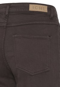 Πίσω τσέπη και μέση σκούρου καφετί τζιν από denim με μπεζ ετικέτα ICHI πάνω από την τσέπη.
