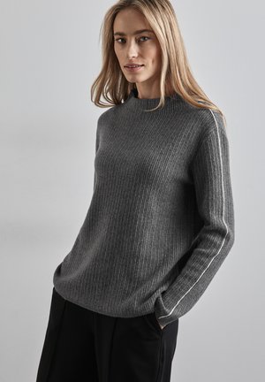 Grauer gerippter Pullover mit hohem Kragen und weißen Seitenstreifen. Lange Ärmel, weiche Textur, lockere Passform, kombiniert mit schwarzen Hosen.