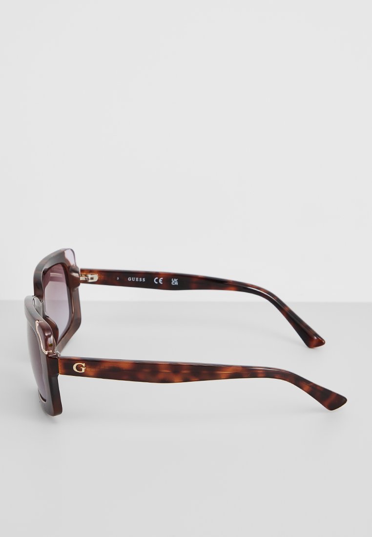 Sonnenbrille mit Schildpattrahmen und lila verlaufenden Gläsern. Verfügt über ein goldenes Logo am Bügel und ein schlankes, kantiges Design.
