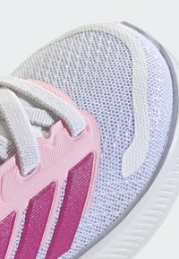 Balta acs sporta apavu ar rozā akcentiem un trim teksturētiem svītrām. Gluda gumijas zole un teksturētas mežģīņu detaļas.