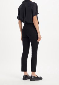 Camisa negra de manga corta combinada con pantalones vaqueros negros de cintura alta, con un corte ajustado y detalles de costura sutiles, complementada con mocasines negros.