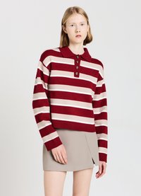 Pull rayé rouge et beige avec col polo, fermeture à l'avant à cinq boutons, poignets côtelés et longueur raccourcie. Assorti à une jupe beige.
