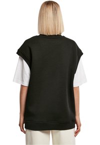 Czarna, luźna bluza z krótkimi rękawami, noszona na białej koszulce, z okrągłym dekoltem i ściągaczem na dole.