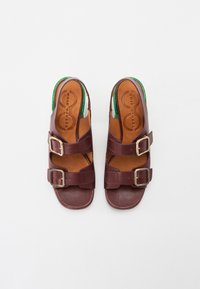 Sandalias de cuero marrón con dos correas ajustables y hebillas plateadas. Plantilla texturizada, diseño de parte trasera abierta, con un acento verde.