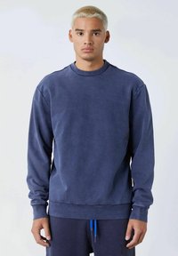 Sudadera azul marino con cuello redondo, mangas largas y puños y dobladillo acanalados. Confeccionada en un tejido suave con una textura lisa.
