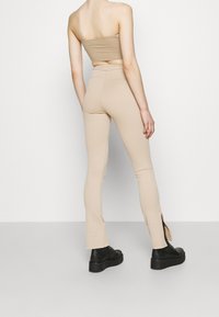 Beige ribbad croptopp kombinerad med åtsittande beige byxor med sidoklipp, bärs med svarta plattformsskor. Slät textur, smal silhuett.