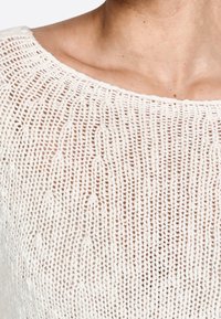 Top de punto en color marfil con un escote amplio. Presenta una textura suelta de tejido abierto y un sutil patrón vertical en toda su superficie.