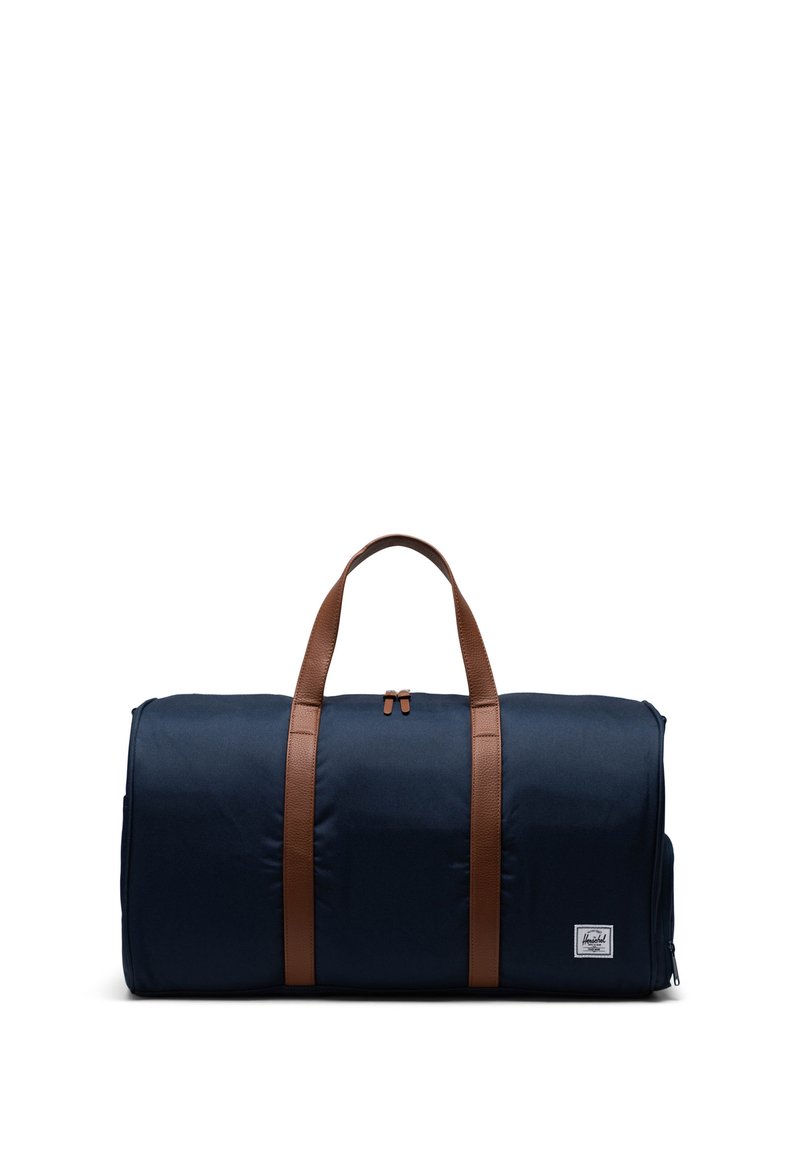 Námořnická látková taška ve tvaru válce s hnědými koženými popruhy, se zipovým uzávěrem a boční kapsou s logem značky.