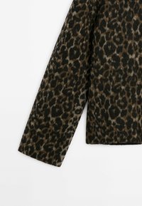 Manche longue d'un manteau à imprimé léopard avec des taches marron, noires et beiges sur un fond blanc.