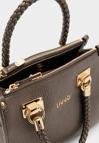 Sac à main en cuir noir texturé avec anse tressée, accents en métal doré, fermeture éclair, et logo de la marque affiché à l'avant.