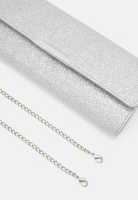 Hopeakimallella varustettu clutch-laukku, jossa on metallinen suljin, sileä pinta ja irrotettava ketjuhihna, jossa on rapu-sulkija.