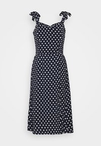 Marineblauwe jurk met witte polkadots, verstelbare strikbandjes, V-hals, aangesloten lijfje en uitlopende rok. Soepele textuur, kniehoogte.