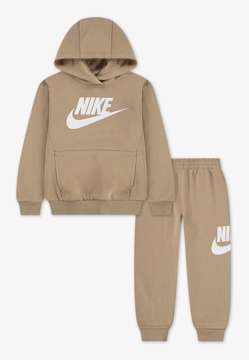 Ensemble de survêtement beige à deux pièces comprenant un pull à capuche avec poche avant et logo Nike blanc, associé à un pantalon avec taille élastique, également avec logo.