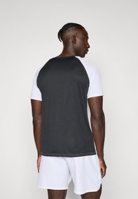 Black and white athletic T-shirt featuring short sleeves, ribbed texture, and a straight hem, paired with white shorts.