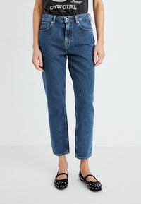 Modre jeans z visokim pasom in ravnimi nogavicami, z rahlim zbledelostjo, ki vključujejo klasično pet žepno zasnovo ter kovinsko zaponko.