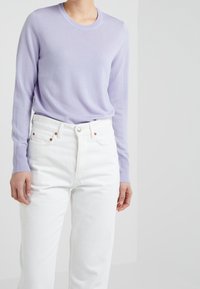 Pull lavande à manches longues en maille douce, associé à un jean blanc taille haute avec une coupe droite et des boutons en laiton en guise d'accent.