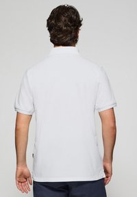 Witte polo met korte mouwen, een gestructureerde kraag en een rechte zoom. Materiaal lijkt glad te zijn zonder zichtbare patronen of accenten.