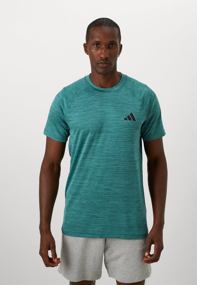 Camiseta deportiva turquesa hecha de tela texturizada, con cuello redondo y mangas raglán cortas. Logo negro en el pecho.