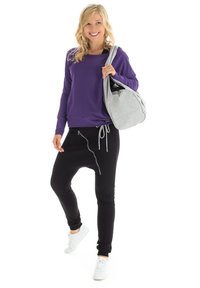 Purple sweatshirt, black joggers with a zipper detail, paired with white sneakers. Grey bag with curved design, held over shoulder.