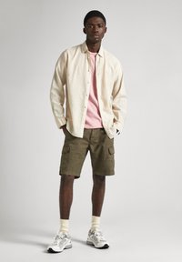 Light beige button-up shirt over a pink t-shirt, olive green cargo shorts, white and gray sneakers, and cream socks.