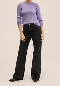 Pull en maille lilas avec un col rond, porté avec un jean noir à taille haute et pattes d'éléphant, complété par des chaussures noires et un fond neutre.
