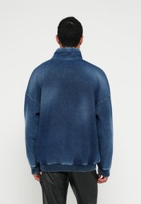 Ohlapen mornarsko moder pulover z rahlim bledenjem, visokim ovratnikom, rebrastimi manšetami in robom. Tkanina ima mehko, teksturirano podobo.