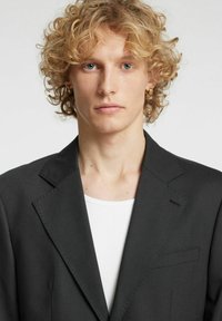 Blazer grigio antracite con design strutturato, rever a lancia e una tasca sul petto. Sotto, è visibile una maglietta bianca con girocollo.