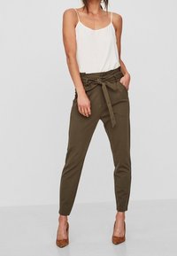 Olivově zelené zúžené kalhoty s vysokým pasem, látkovým páskem a bočními kapsami, zkombinované s bílým topem na ramínka a hnědými vysokými podpatky.