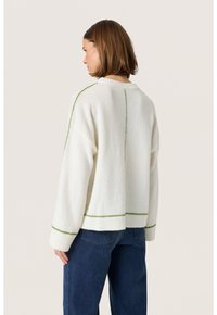 Hvid strikket sweater med grøn accenttråd, der har en afslappet pasform, ribbet kant og dropped skuldre. Bæres med blå jeans.