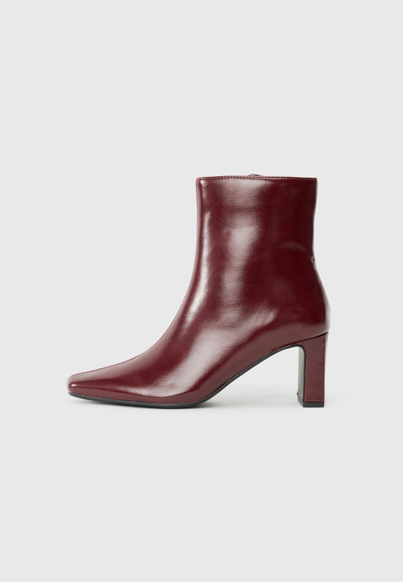 Cizma de gleznă din piele bordeaux, cu vârful ascuțit, textură lucioasă și toc pătrat. Prezintă o suprafață netedă și un design minimalist.