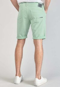 Shorts vert menthe avec des revers, dotés de deux poches arrière et d'un petit détail noir, portés avec des baskets blanches.