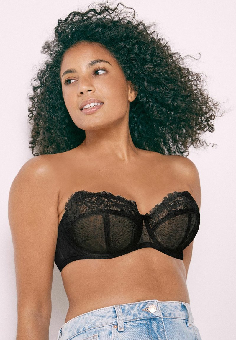 Black lace bra with sheer mesh panels, underwired cups, and decorative lace trim. Features a bow accent at the center and adjustable straps.