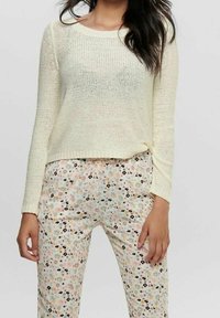 Strickpullover in Creme mit langen Ärmeln und rundem Ausschnitt, kombiniert mit pastellfarbenen Hose mit Blumenmuster, die schwarze und gelbe Akzente aufweist.