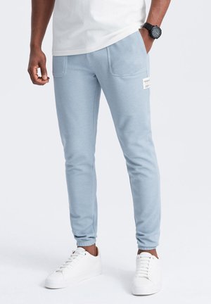 Pantalones de chándal azul claro hechos de una mezcla de algodón, con bolsillos laterales, puños acanalados y un detalle de etiqueta en el muslo izquierdo. Combinados con zapatillas blancas.