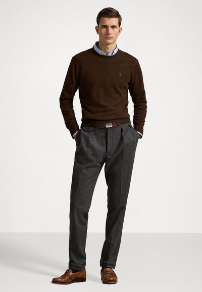Suéter marrón, pantalones grises con pliegues, zapatos de cuero marrón. El conjunto incluye una camisa con cuello debajo del suéter y un cinturón con una hebilla de plata.
