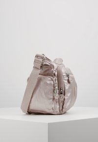 Mała metaliczna różowa torba na ramię z regulowanym paskiem, przednią kieszenią na zamek i srebrnym breloczkiem w kształcie małpy na białym piedestale.