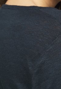 Dark blue knit textile with a smooth texture, featuring a rounded neckline and a subtle sheen, closely cropped to show the fabric detail.