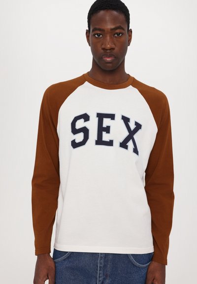 White long-sleeve t-shirt with brown raglan sleeves and bold navy text reading "SEX" across the front. Cotton material, relaxed fit.