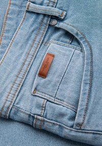 Ljusblå denimtyg med kontrasterande orange sömmar, med en liten brun läderlapp och en detalj med framficka.