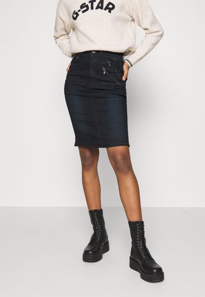 Zwarte denim kokerrok met een aansluitende pasvorm, voorzakken met ritsen en een knielange snit. Gecombineerd met zwarte veterboots.