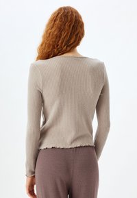 Ribbet langærmet top i lys beige med en subtil bølget kant. Blød tekstur og tætsiddende design, parret med løse, matchende bukser.