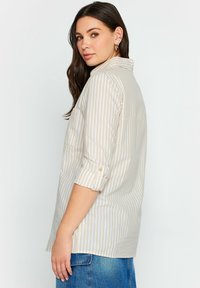 Gestreifte Bluse in Beige und Weiß mit einem kragenlosen Hals, hochrollbaren Ärmeln und einem lässigen Schnitt mit einem Rückenpasse-Detail.