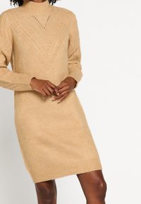 Robe-pull en tricot beige clair avec un col montant, présentant un yoke à motif et des poignets et ourlet côtelés, réalisée en tissu doux et texturé.