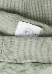 Jasnozielona dzianina o fakturowanym wykończeniu, z białą tkaną metką zabezpieczoną przezroczystym guzikiem. Dzianina jest ściśle tkana z prążkowanym brzegiem.