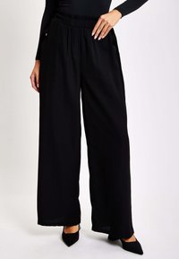 Wide-leg black trousers made of flowy fabric with an elastic waistband, featuring side pockets and a smooth texture.
