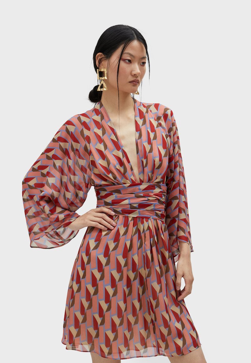Sheer, kuviollinen mekko, jossa on geometrisia muotoja punaisena, vaaleanpunaisena ja sinisenä, leveät hihat ja vaikuttava vyötärösuunnittelu.