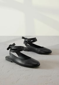 Mustad musta nahast slingback jalatsid, millel on ümar nina, lõikekujundus ja ümberpööretav pahkluu rihm. Tasane tallatüüp sujuva tekstuuriga.