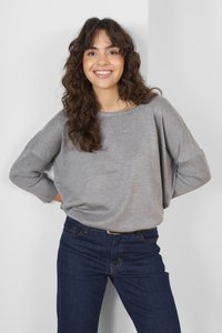 Lys grå oversized sweater med ribbet ærmer, parret med mørkeblå jeans med orange syninger. Glat stoftekstur.