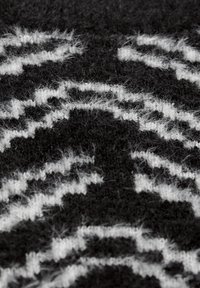 Pull en laine tricoté avec une base noire et des motifs abstraits blancs. Surface texturée avec des fibres douces et une apparence confortable.